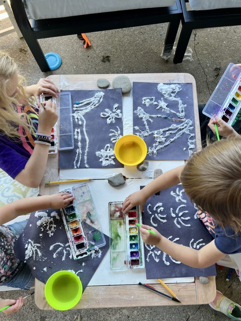 Overhead view of kids painting fireworks made of glue and salt with watercolors.