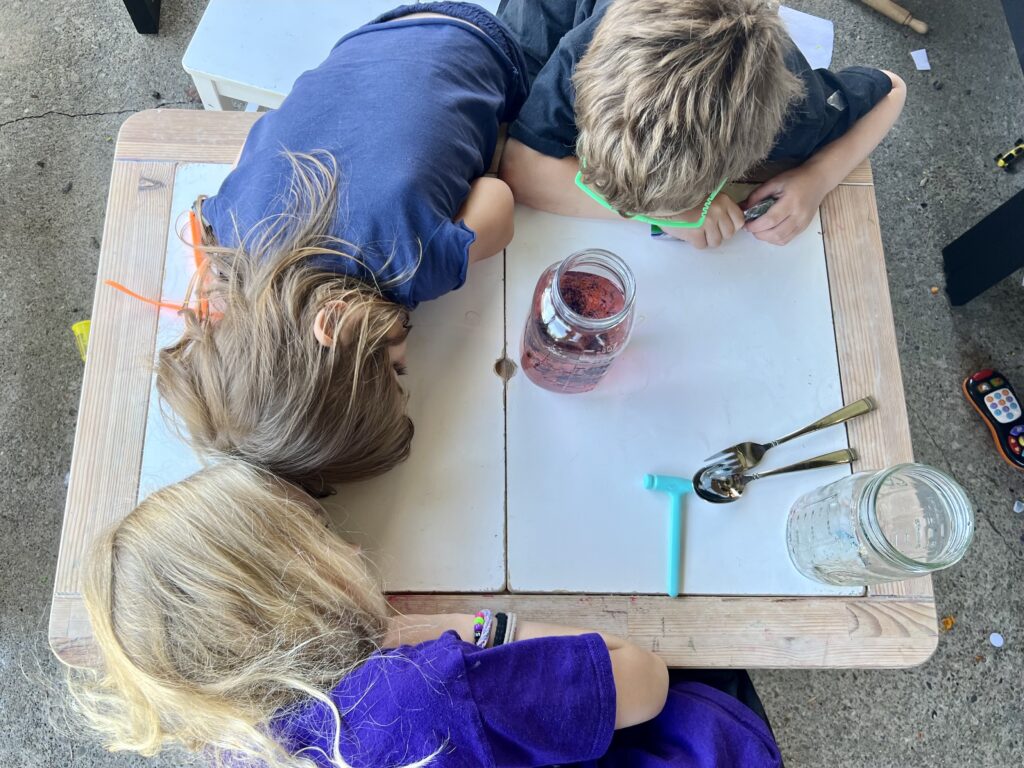 Kids looking at a glass jar filled with food coloring, water, and oil