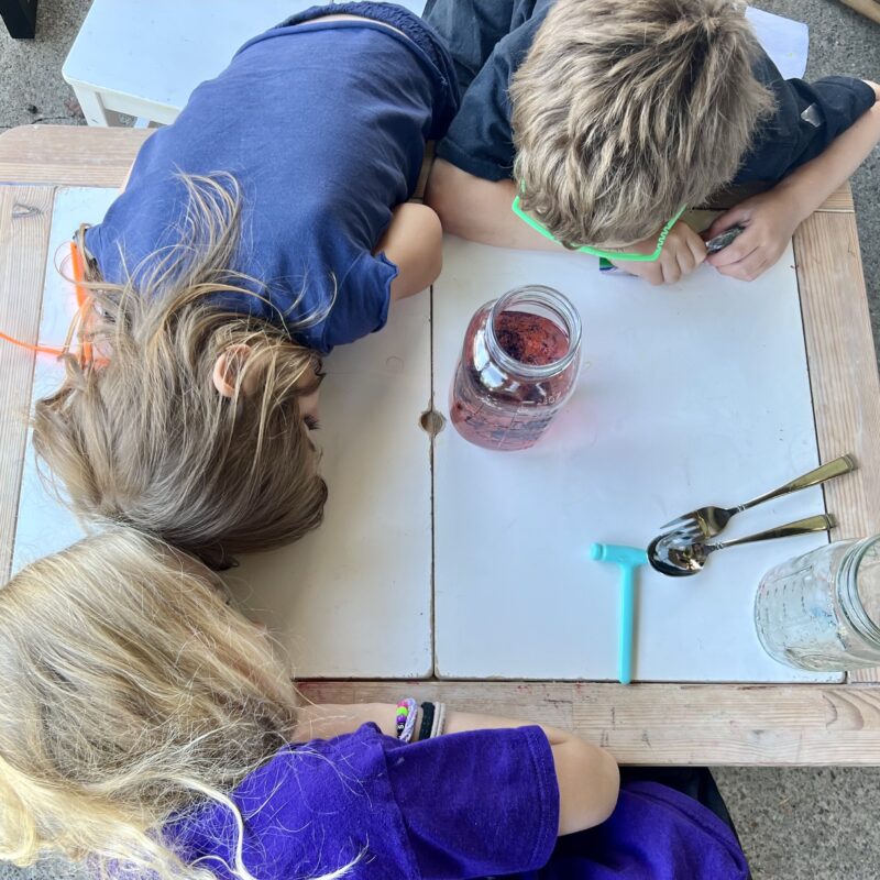 Kids looking at a glass jar filled with food coloring, water, and oil