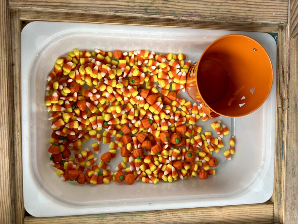 a white bin with an orange jack o lantern bucket surrounded by candy corn and candy pumpkins