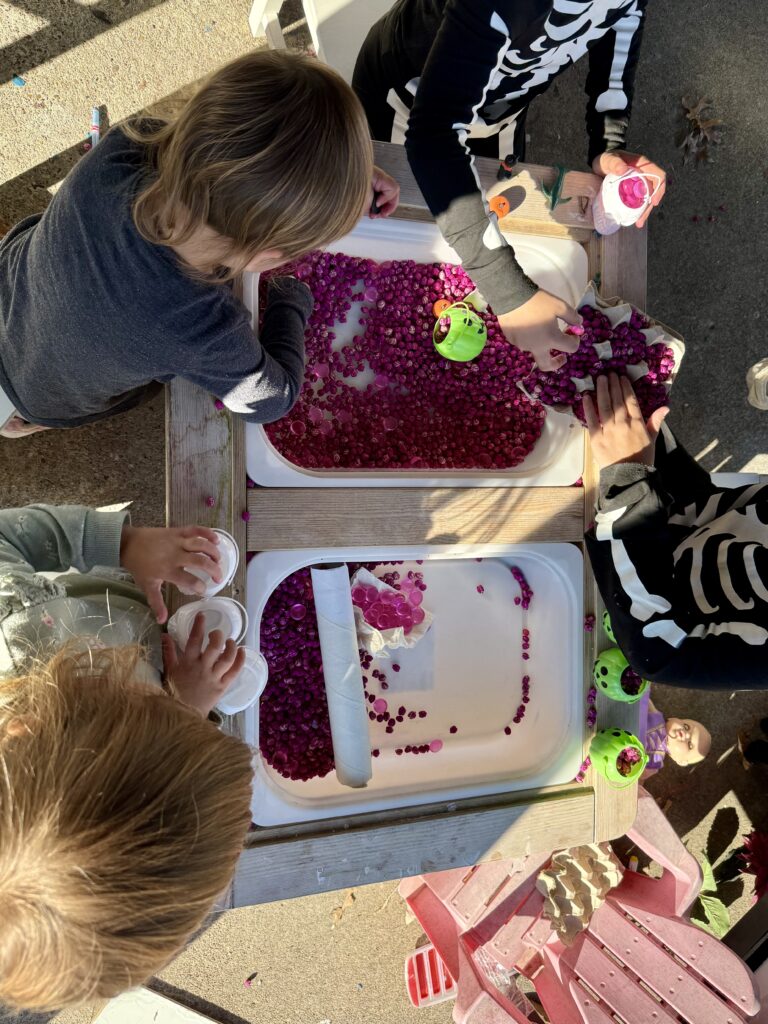 Four children playing in a sensory bin for breast cancer awareness filled with dyed pink chick peas and pink flat marbles