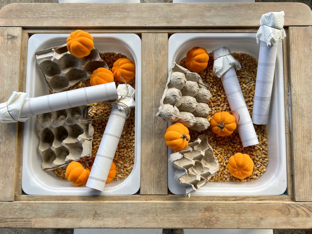 A fun fall sensory bin with two buckets filled with paper towel rolls, egg cartons, pumpkins, and corn kernels.