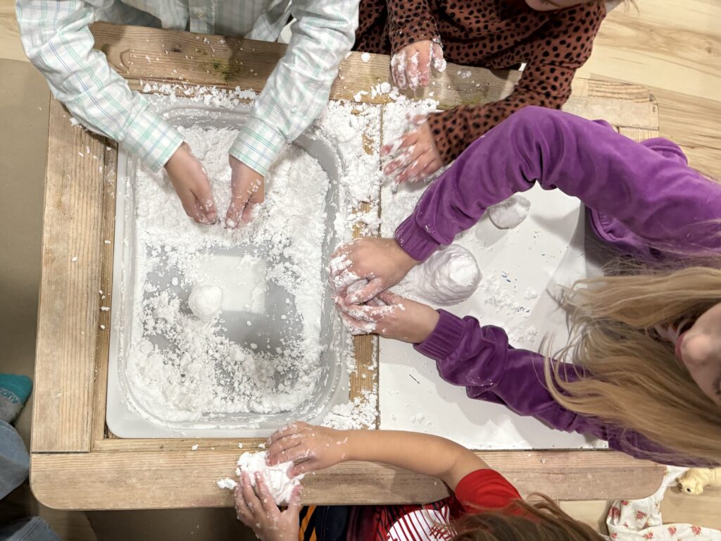 Children playing in a sensory bin filled with instant snow, molding it into shapes. 