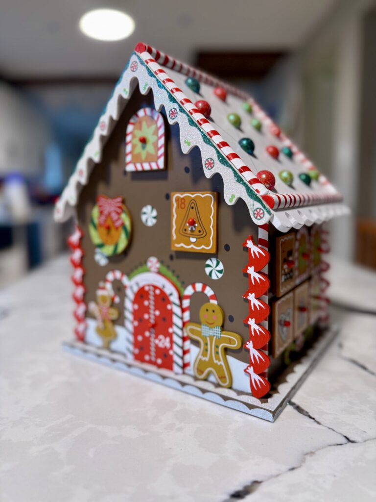 Photo of a gingerbread house with 24 windows and doors that are pull out boxes to make an advent calendar: house is brown with lighter brown, red, green decorations and windows