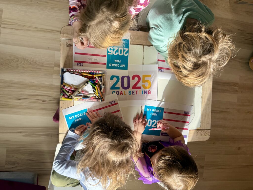 4 kids sitting at a table with papers for 2025 goal setting, each with goals for individual, family, and fun