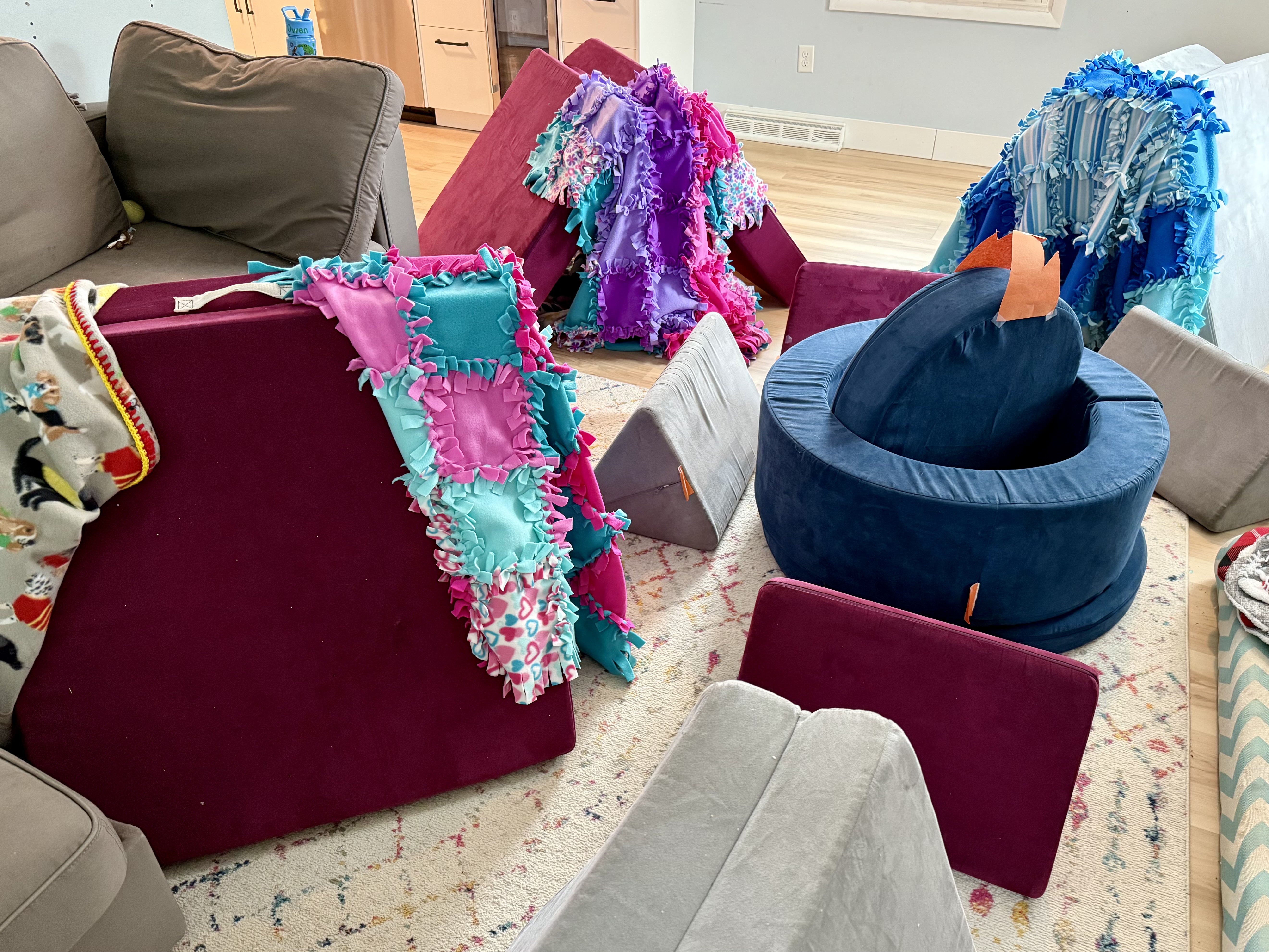 Children play couches set up as tents around a pretend campfire, blankets laying over the openings to create doors