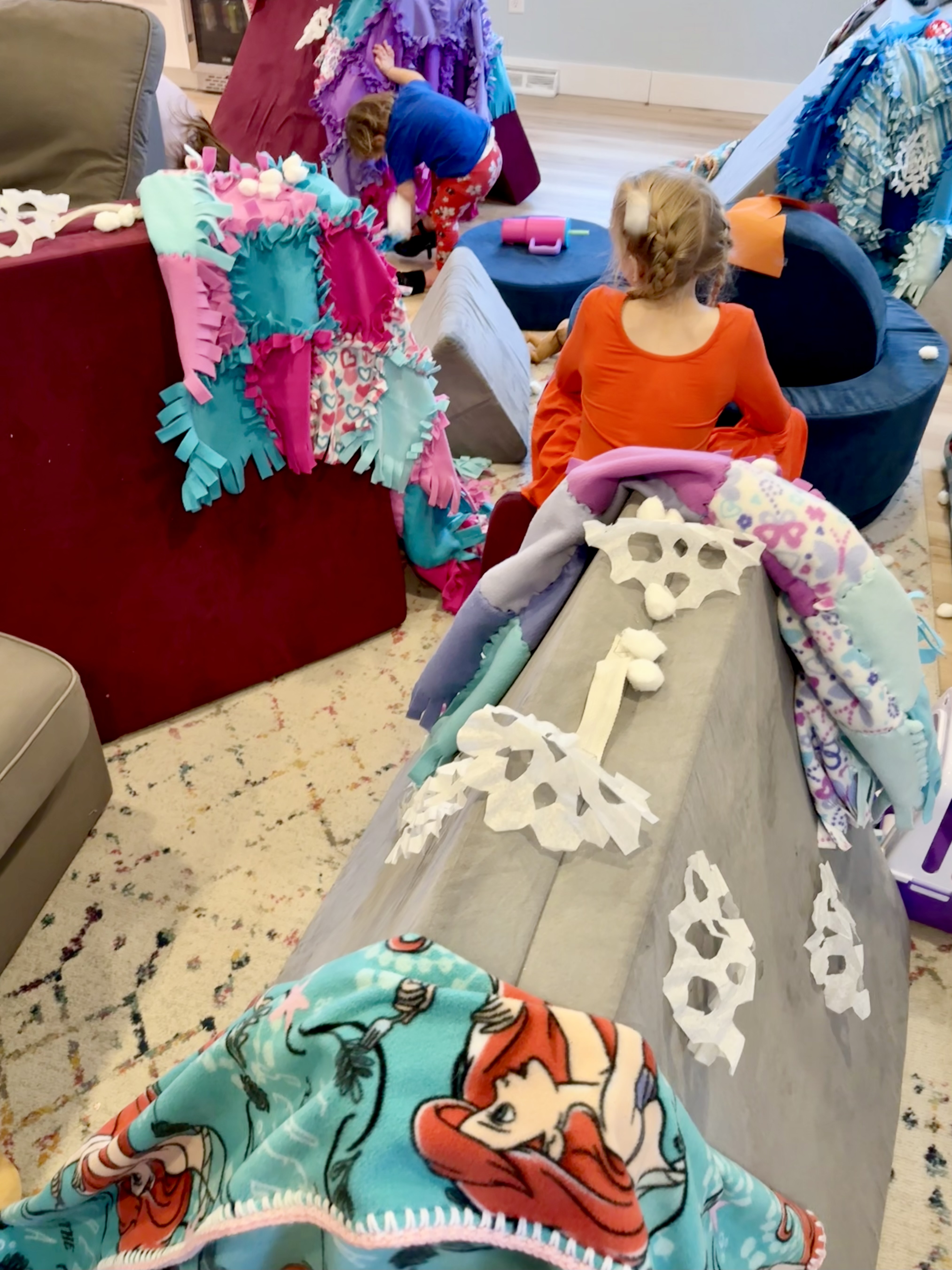 Children sitting in tents and around a campfire all build from children's play couches - covered in snowflakes with falling cotton balls.