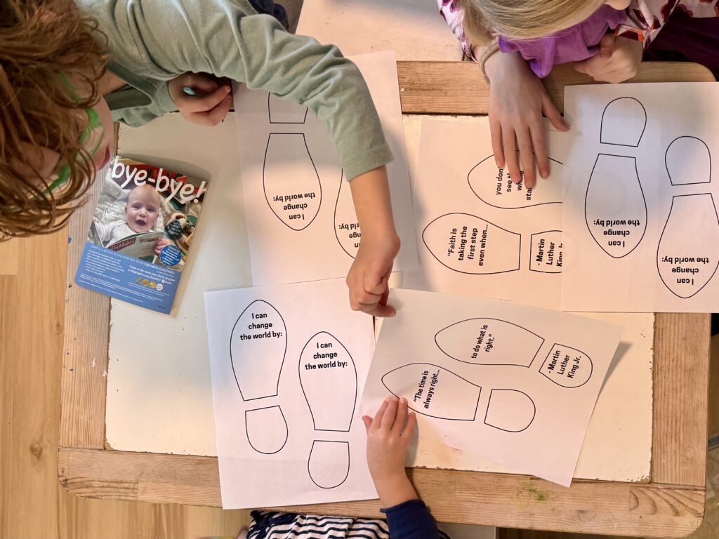 Children reaching across a table with shoe prints. Some shoe prints with quotes from Martin Luther King, Jr. and others with sayings of I can change the world by: 