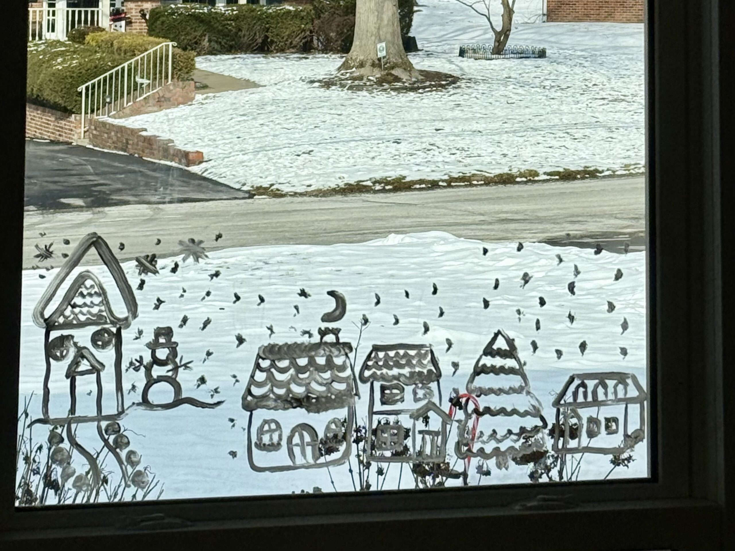 Winter Village Window Painting: A window painted with a winter scene similar to a winter village, 4 houses, a snowman, and a tree under a night sky.