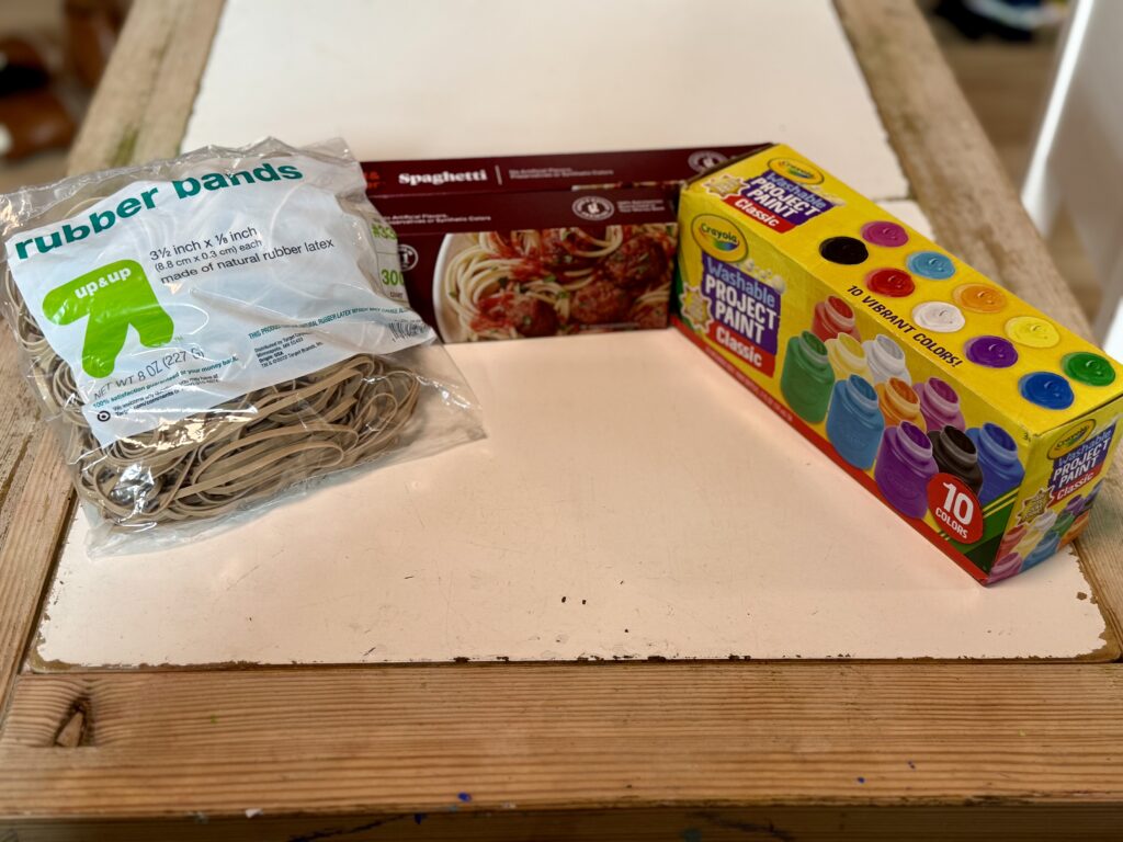 Supplies for making process art to paint with spaghetti: rubber bands, spaghetti noodle boxes, paint