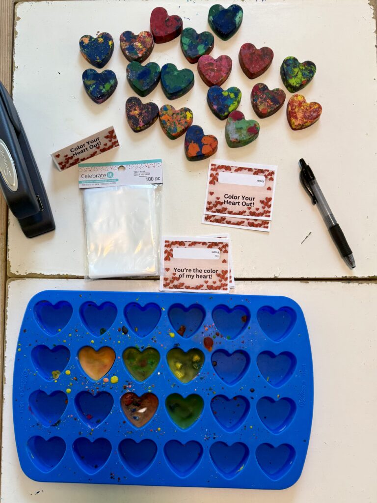 Supplies to make heart shaped crayons: silicone heart mold, bag toppers that read "Color Your Heart Out," clear plastic bags, pen, heart shaped crayons, and a stapler