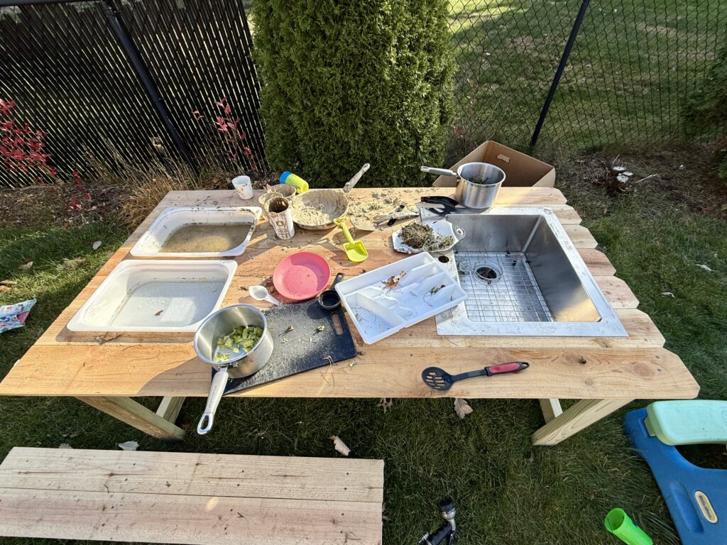 An outdoor mud kitchen covered in kitchen utensils, pots, mud and water. 