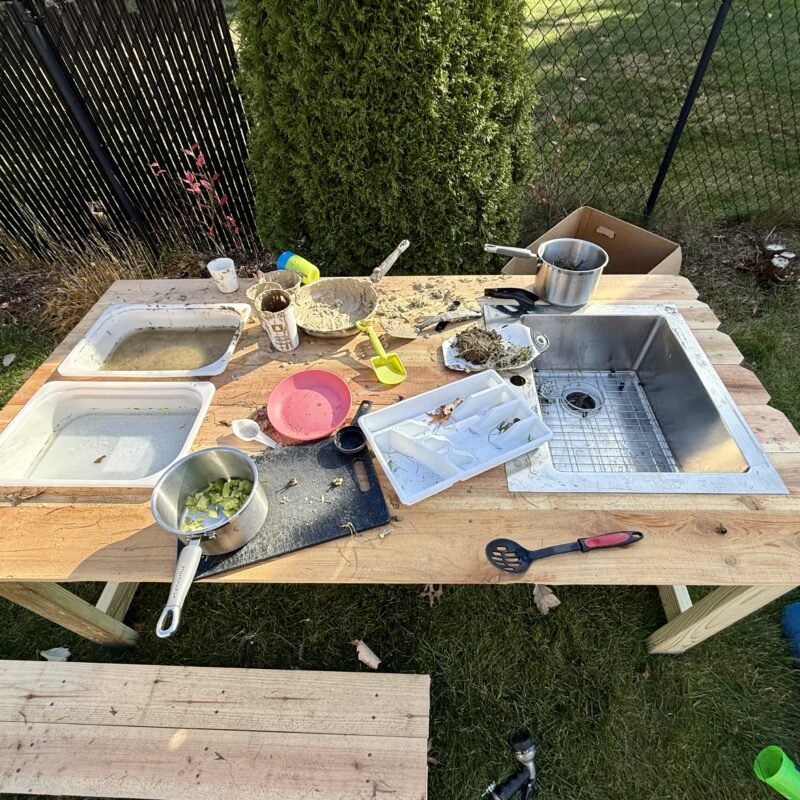 An outdoor mud kitchen covered in kitchen utensils, pots, mud and water.