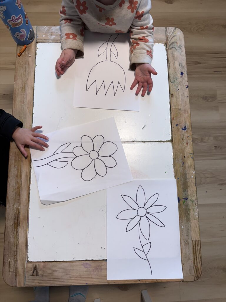 Kids hands around white paper with the outline of flowers drawn in black