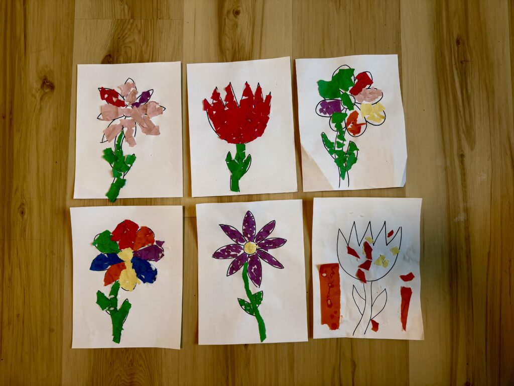 6 white pieces of paper laying in 2 rows. Each with a flower on it, decorated with small pieces of construction paper torn to fit within the flower outline