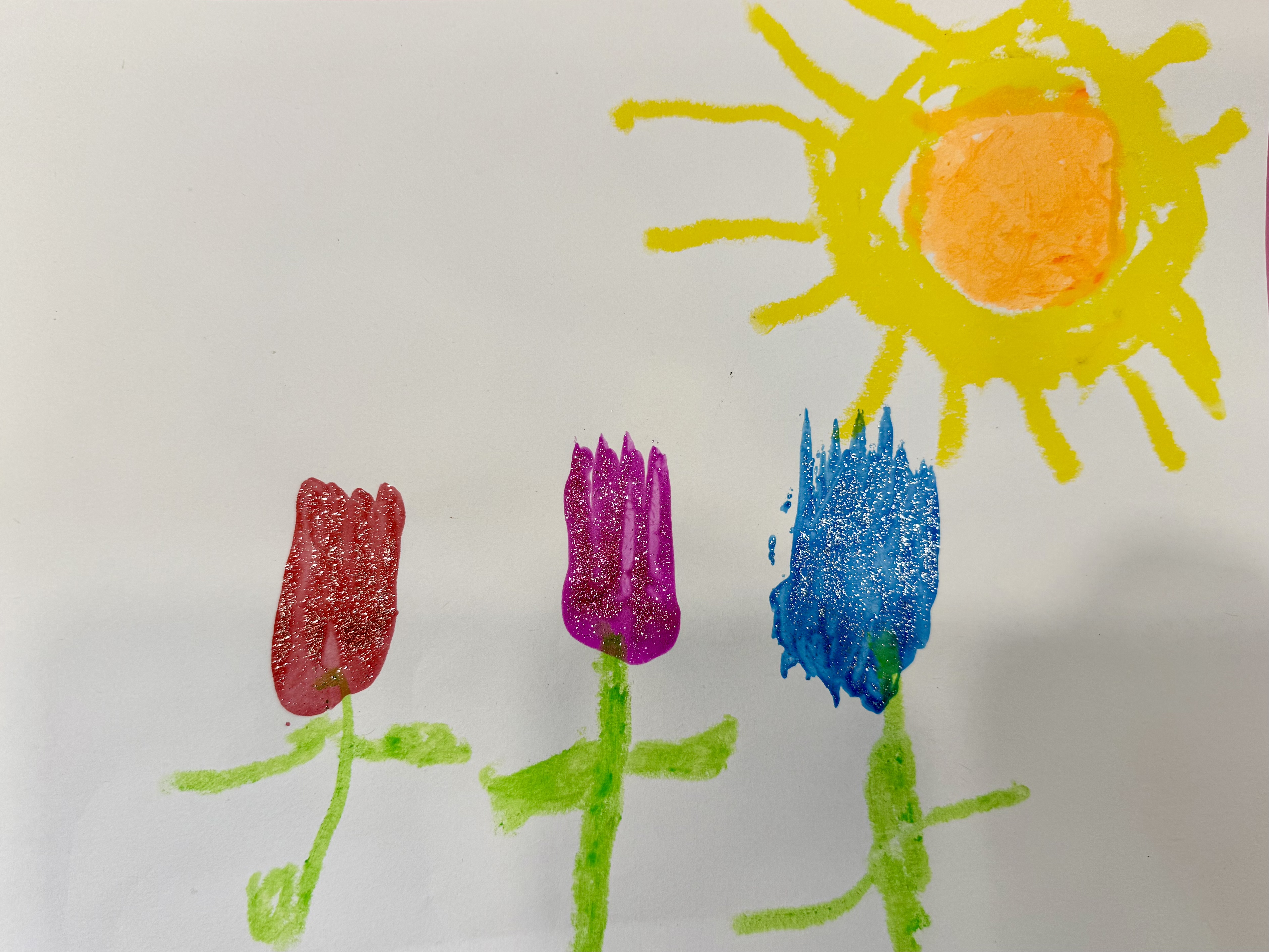 Photo of 3 tulips and a sun, the tulips are pink, red, and blue with glitter. There is a sun made of yellow and orange in the top right corner. They are fork tulip art, the flower portion of the tulip is made from a fork stamp.