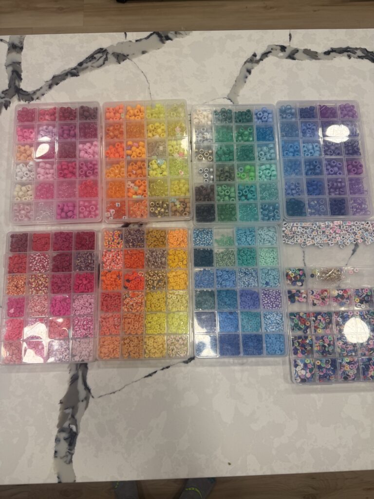 A photo of multiple beads in cases on a counter, ready to make friendship bracelets. Predominantly in rainbow order.