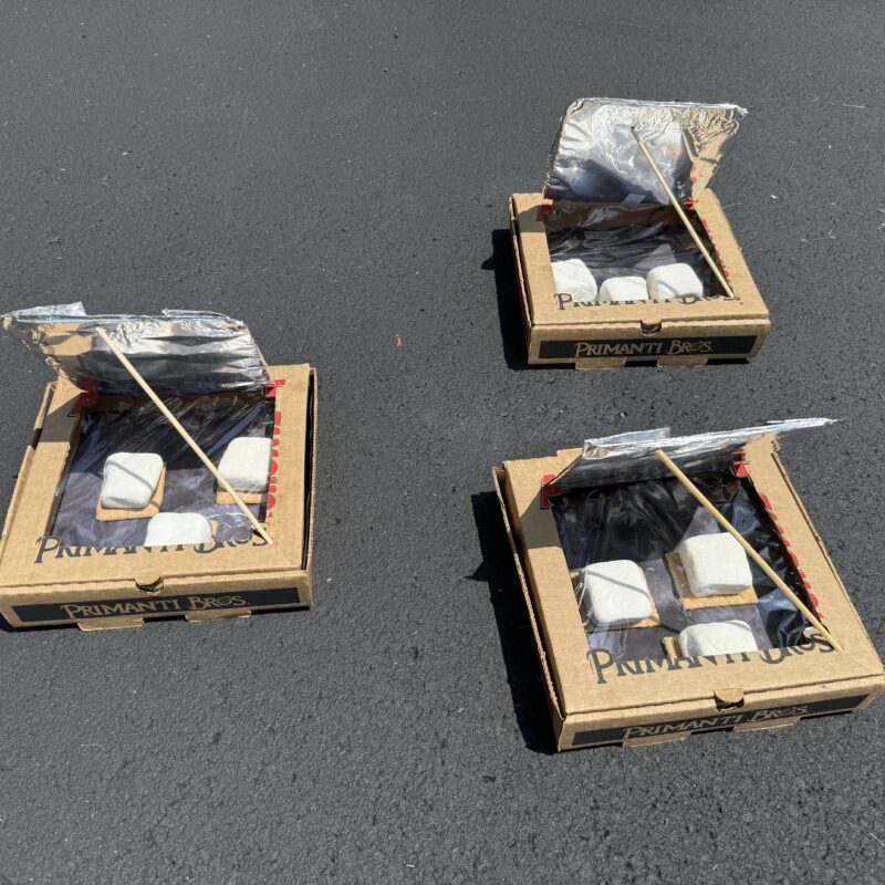 Solar S'mores Oven: pizza boxes with aluminum foil reflecting the sun into the box. Graham crackers with marshmallows on top baking in the sun.